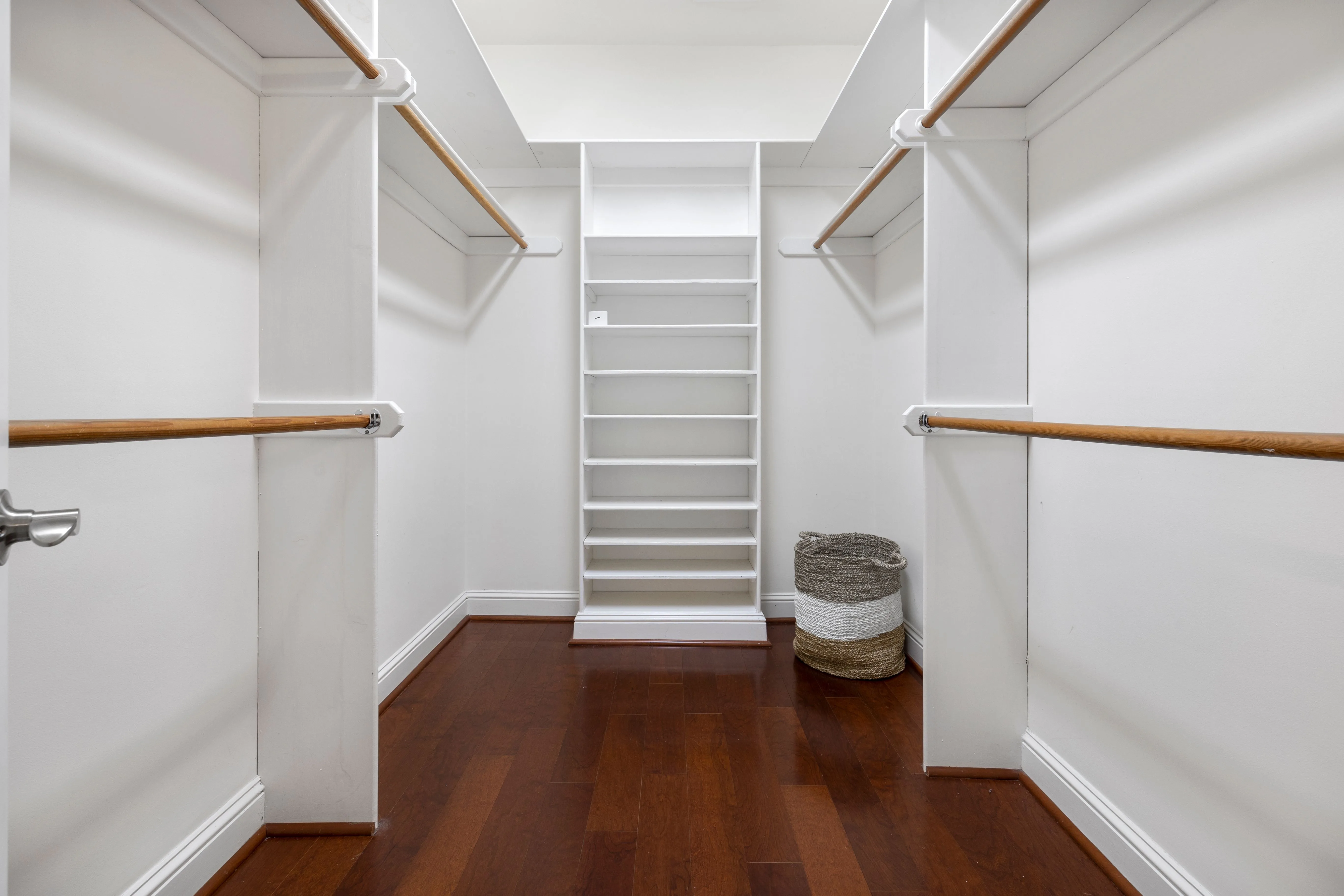 Minimalist empty walk-in closet featuring wooden floors, built-in shelves, and hanging rods, representative of a finished closet organizer