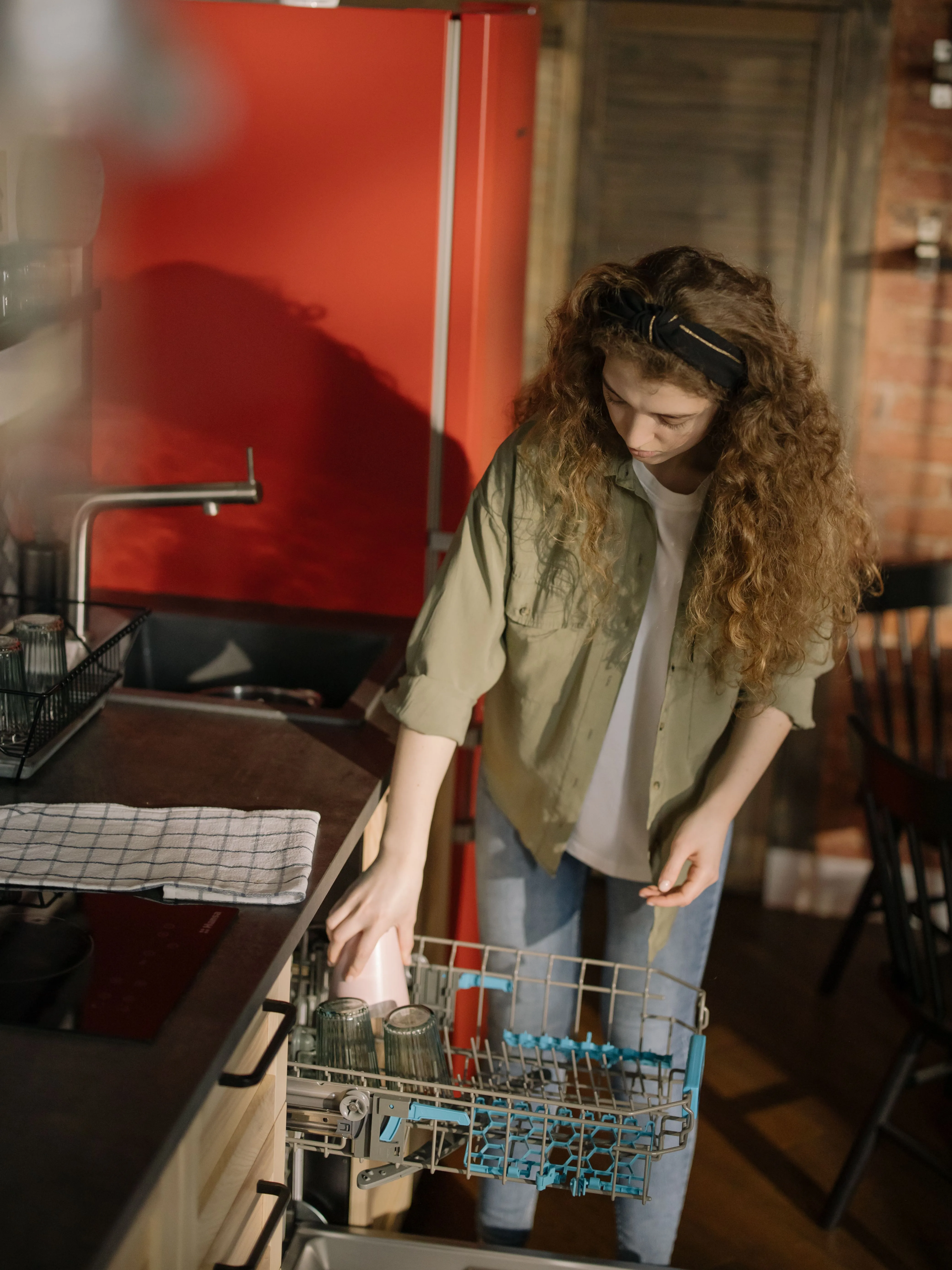 Person loading dishes into an open dishwasher rack, in-use household scene.