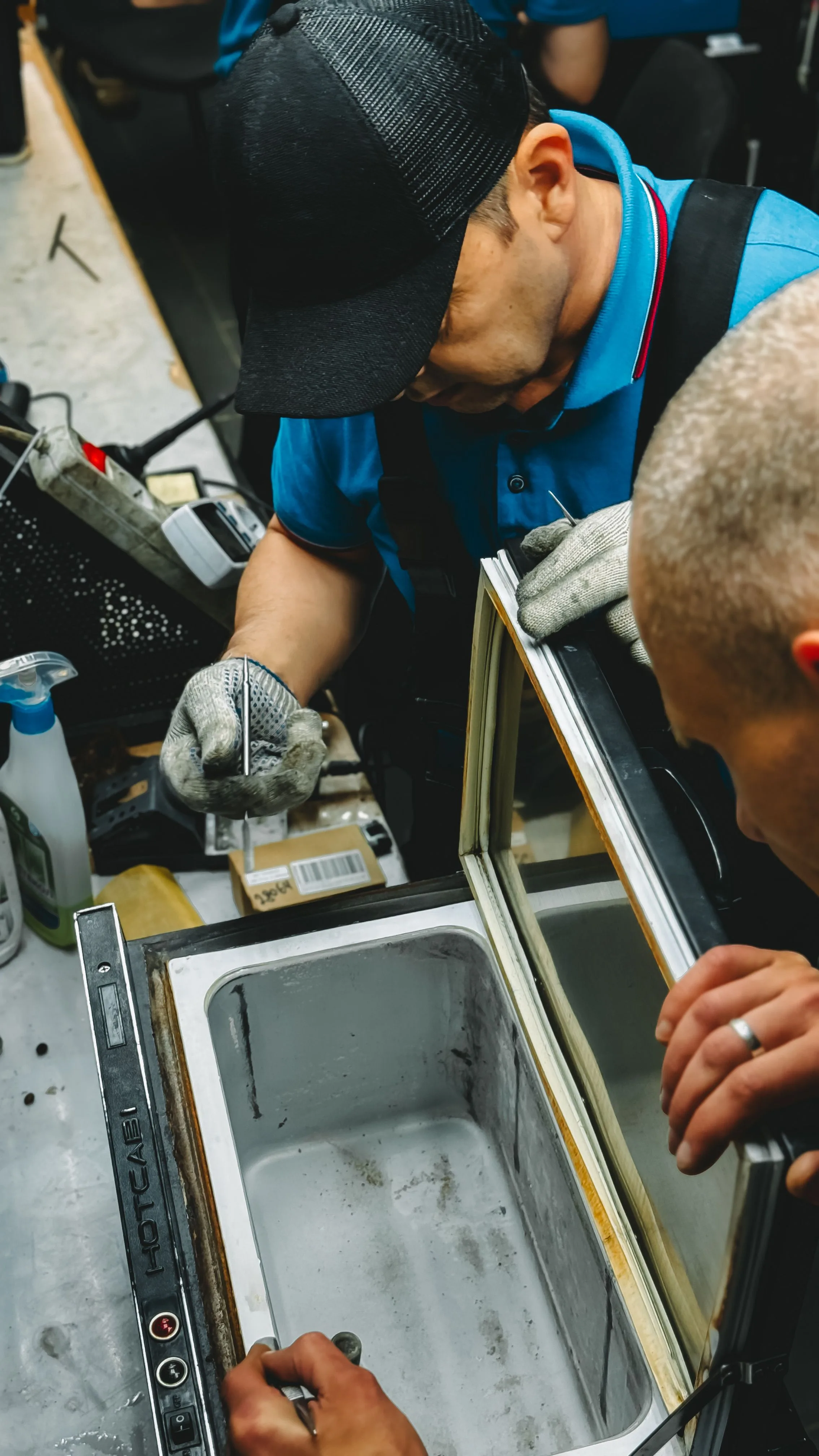 Technician working on the back and mechanical components of a refrigeration unit, illustrating coil-cleaning maintenance.