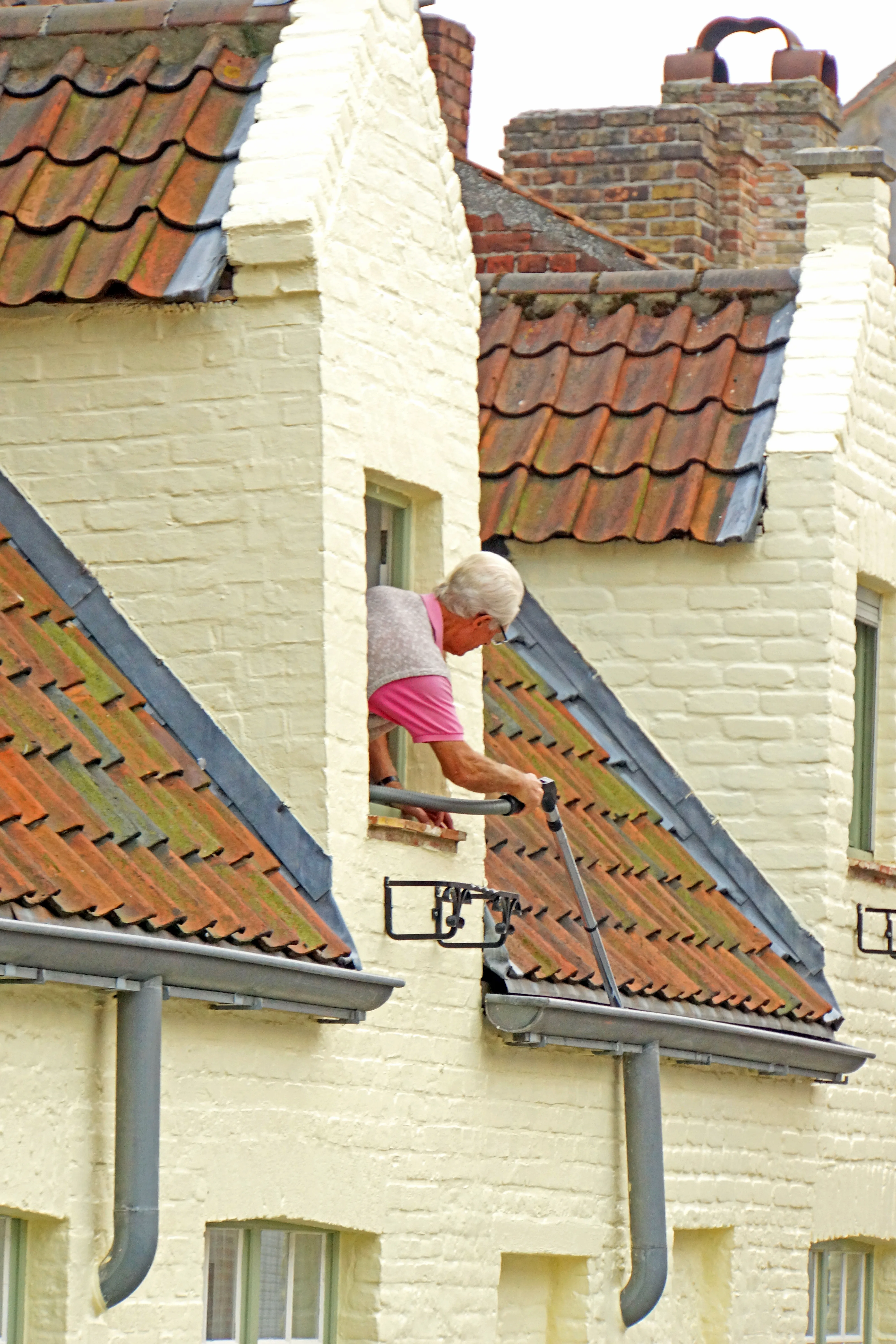 Worker using a vacuum-style tool to clean debris out of a roof rain gutter.