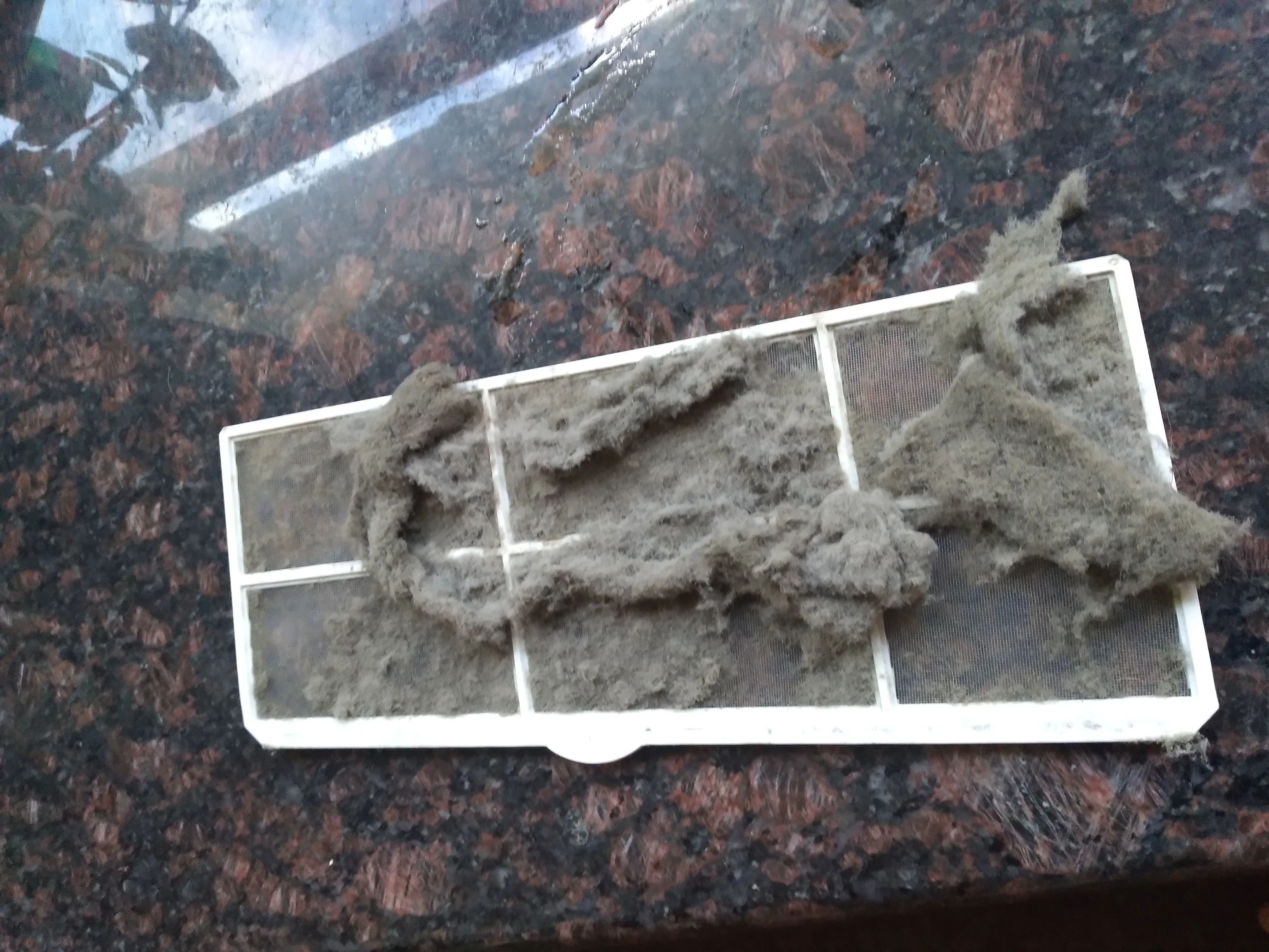 A dirty, dust-clogged air conditioning filter that needs to be replaced, close-up photo.
