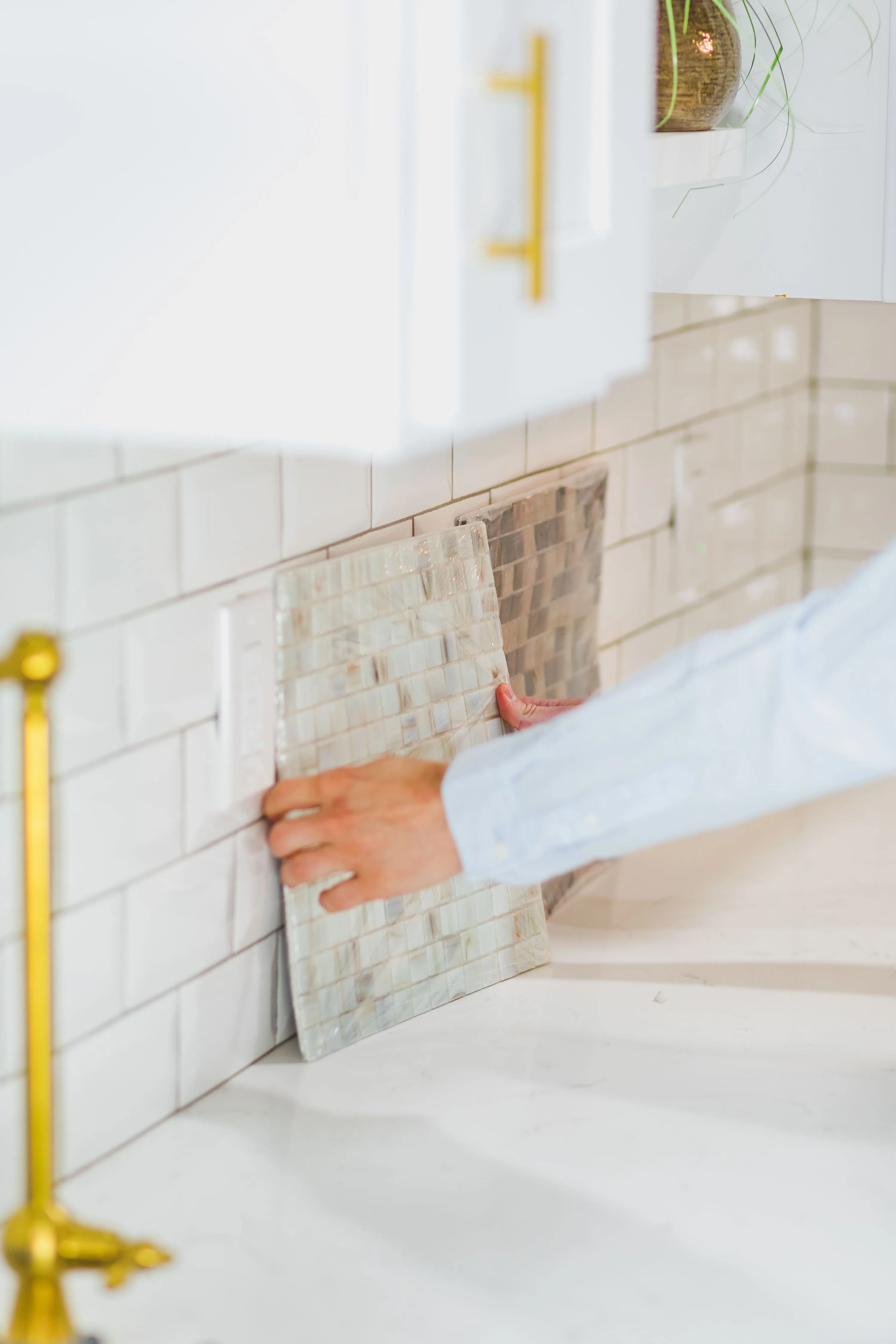 Person installing tile backsplash in a bright, modern kitchen setting, mid-installation.
