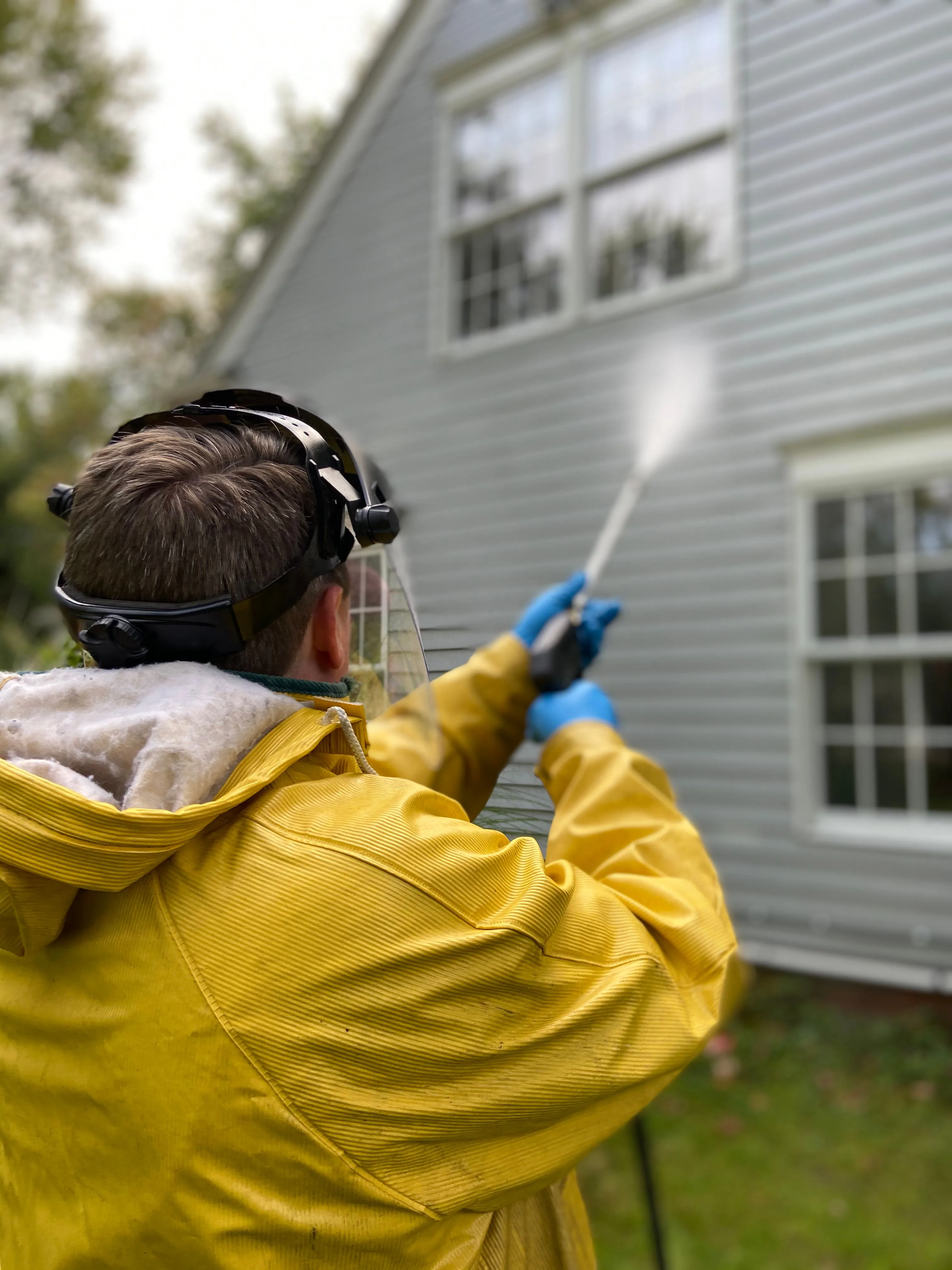 Person actively pressure washing an exterior surface with a high-pressure hose wand, illustrating the in-progress cleaning technique used on decks.