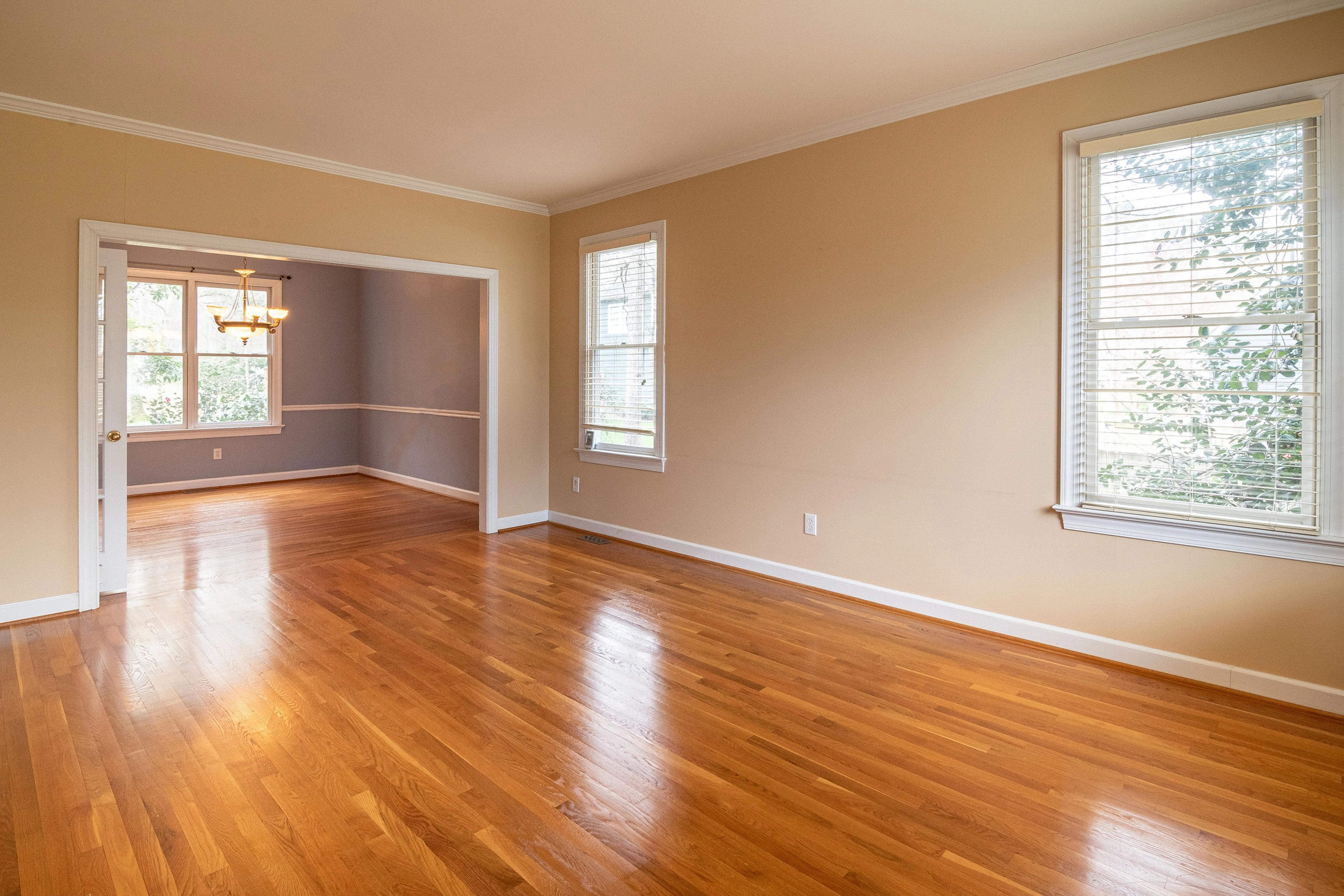 Bright empty room with smooth, evenly finished wood floors and large windows, representative of a refinished hardwood floor