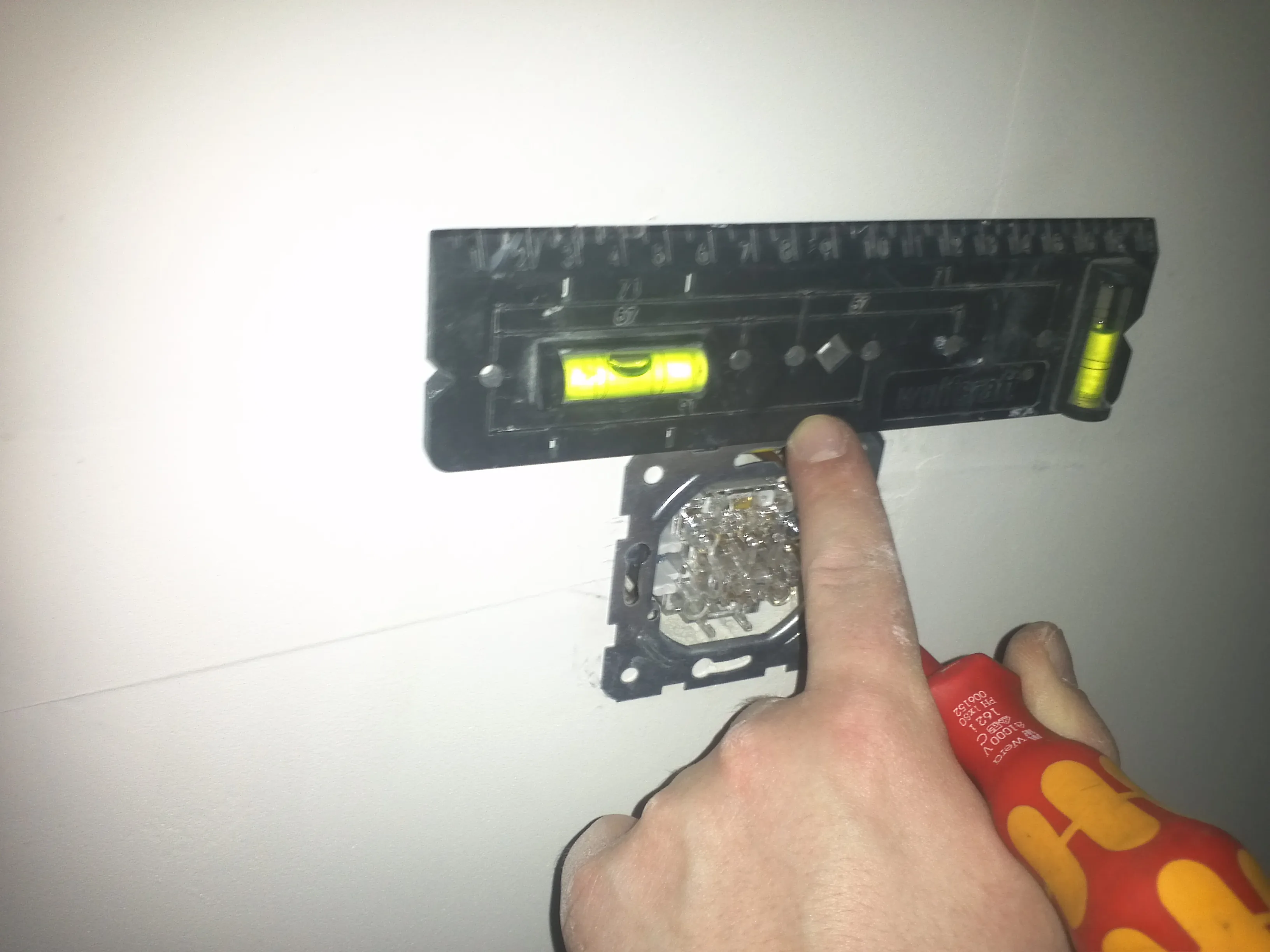 Electrician installing a wall light switch into an electrical box, wires visible mid-process.
