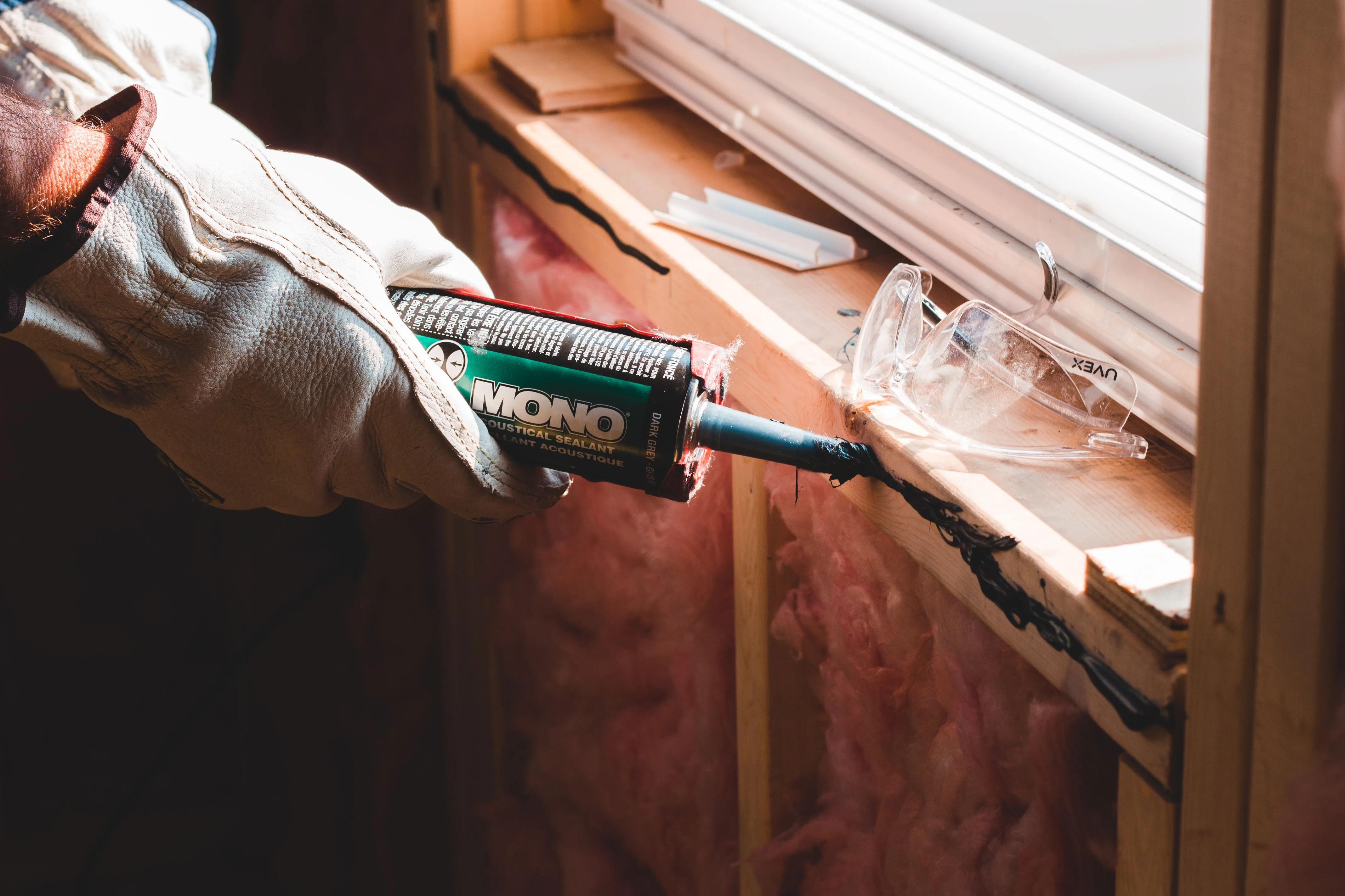 Close-up of a worker applying sealant along a window frame seam during a renovation project.