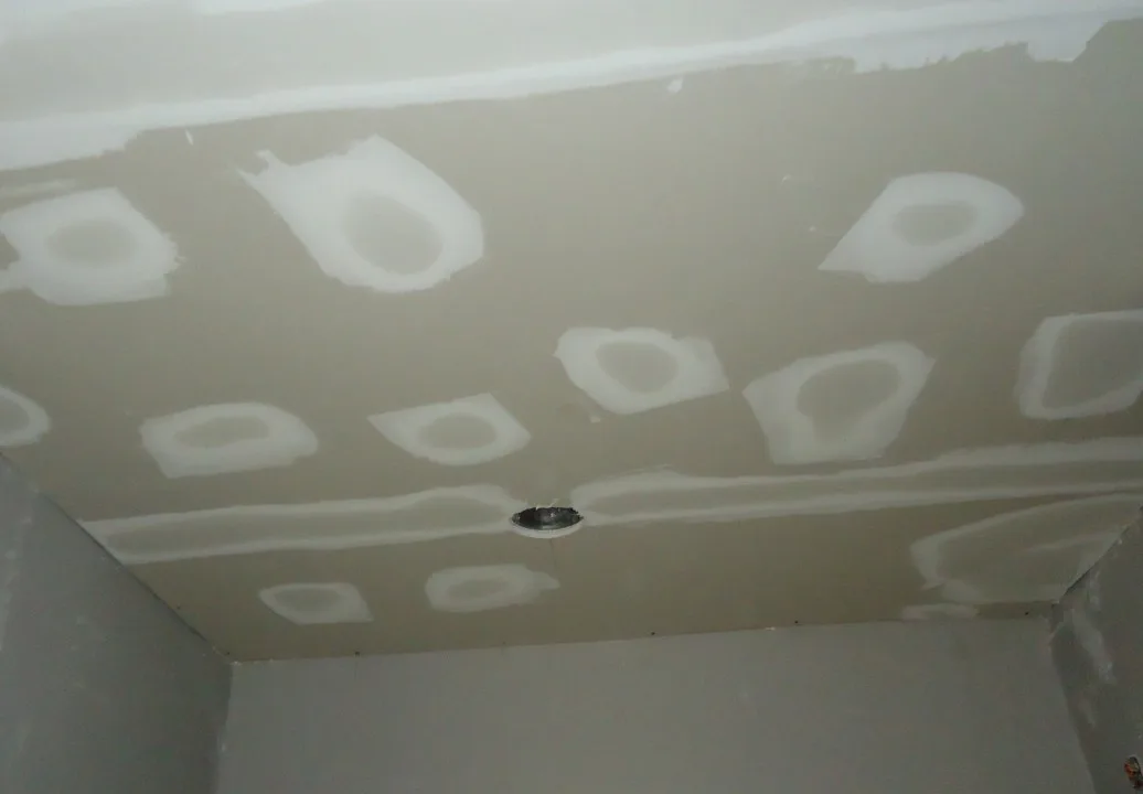 Spackling compound being applied to cover nail holes and tape joints between drywall sheets during a renovation.