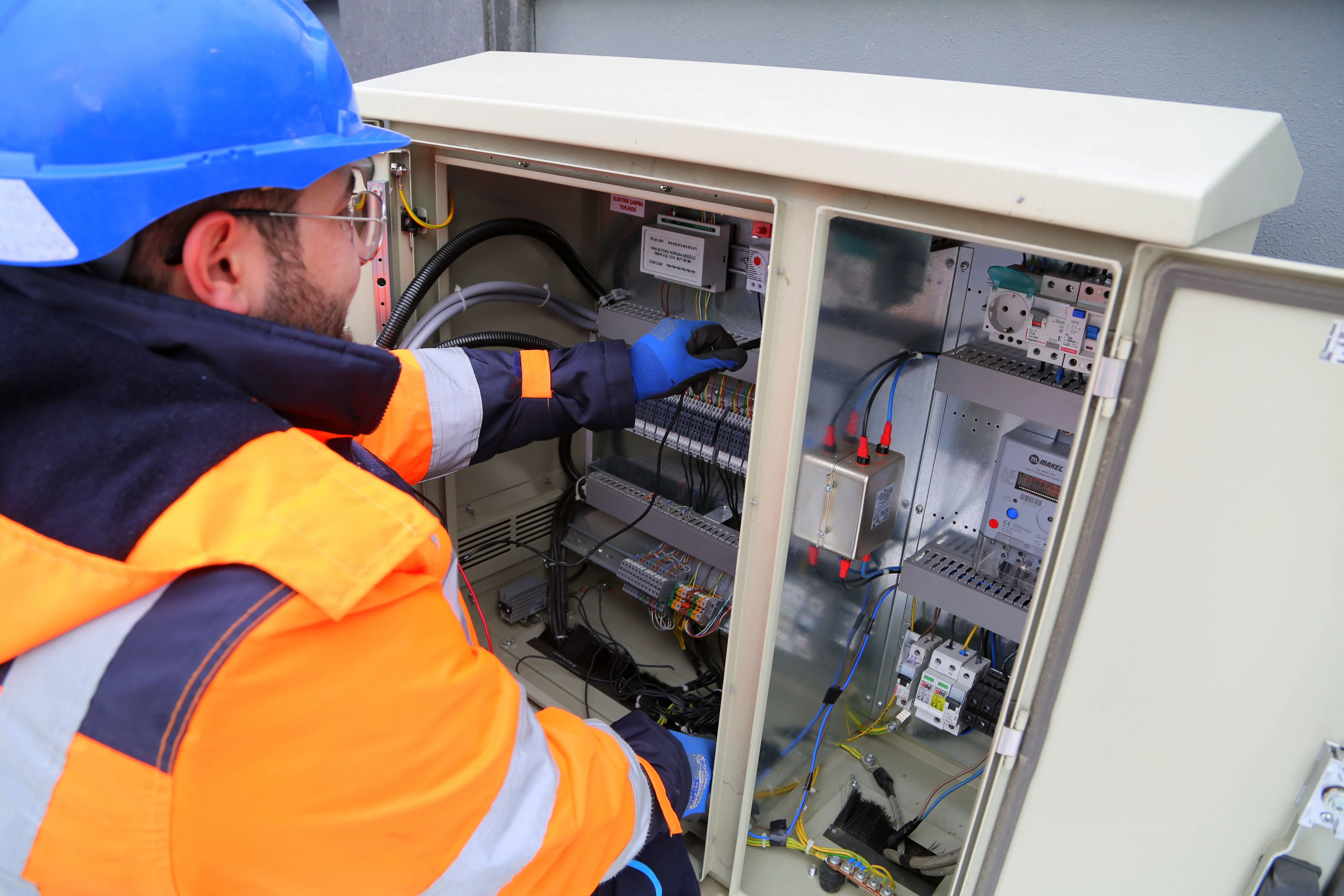 Electrician working at an open residential fuse/breaker box, inspecting wiring.
