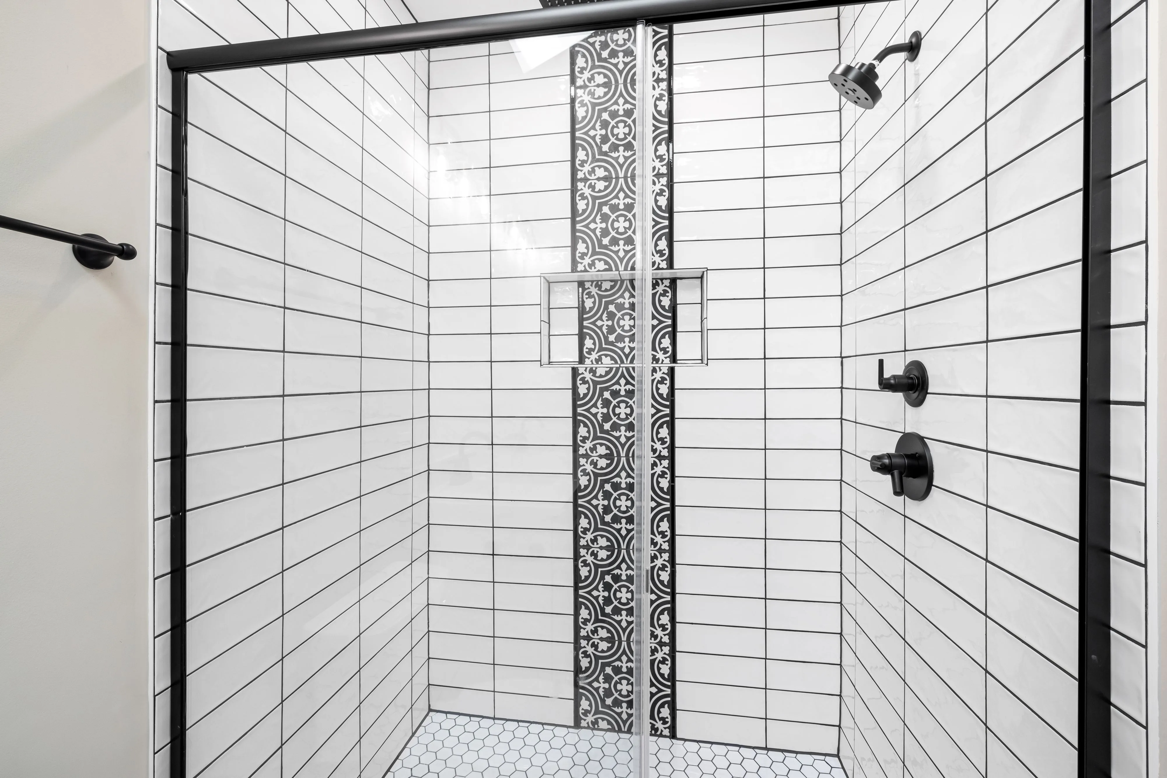 Finished shower stall with white subway tile walls and a black patterned accent wall.